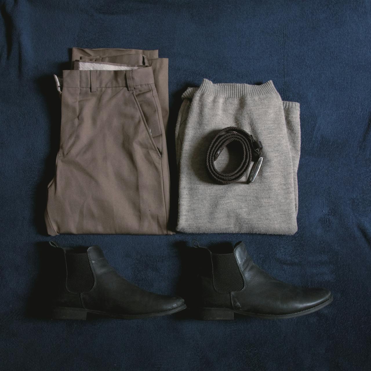 services-01 Men's clothing ensemble including trousers, sweater, boots, and belt arranged on a blue surface.